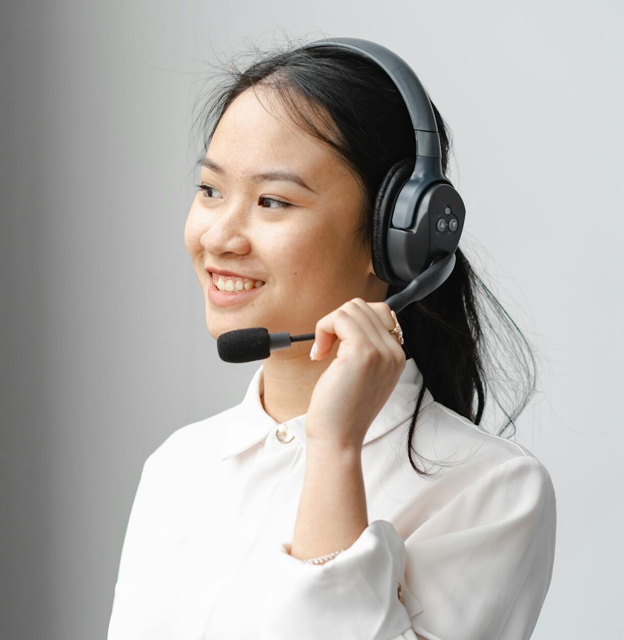 Smiling Asian woman with headset providing customer support in an office setting.